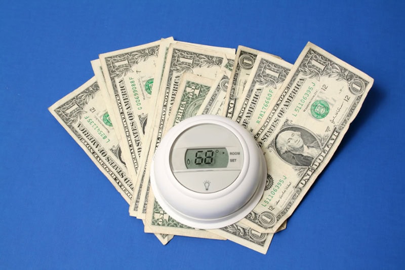Spring Money-Saving Tips. Photo of a thermostat on top of a pile of cash with a blue background.