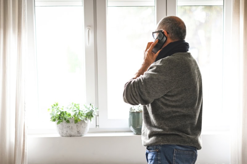 Why Won’t My Furnace Stop Running? Photo of a man talking on his phone, looking out the window seemingly upset.