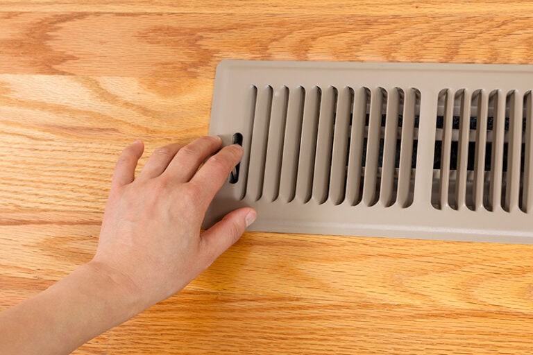 female hand opening up heater floor vent with Red Oak Floors in background.